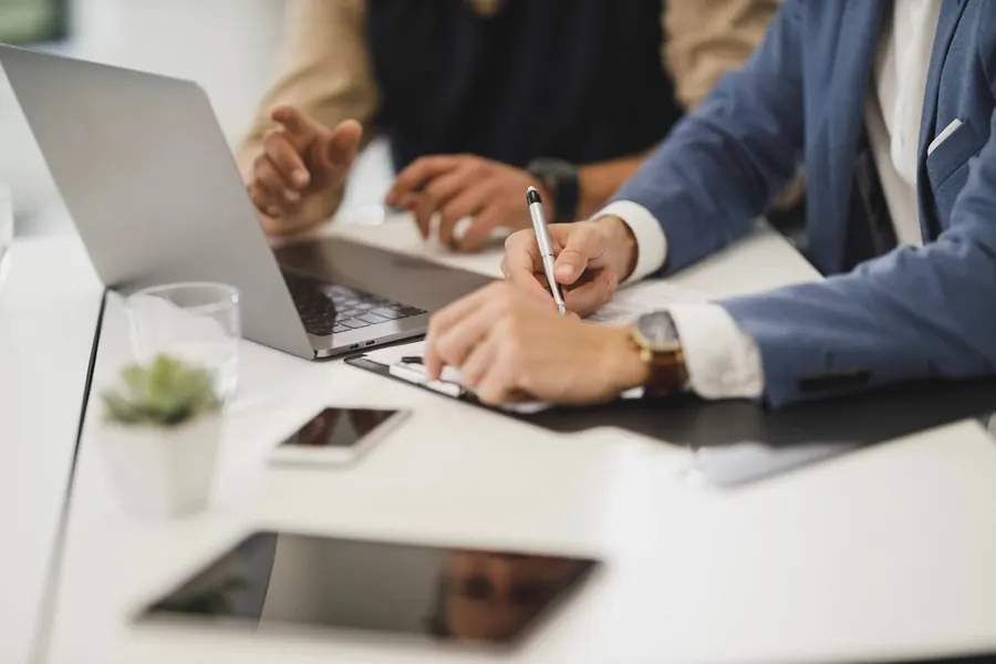 Professional signing documents at a desk next to a laptop
